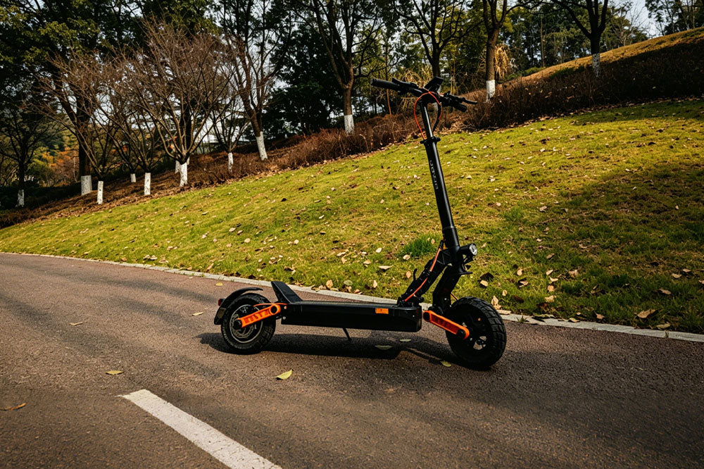 Black electric scooter with orange accents parked on paved park road with green hillside backdrop