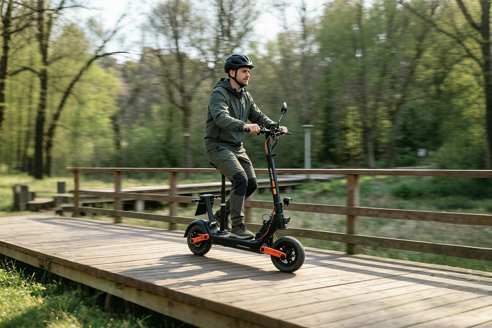 Male rider on orange accent seated folding electric scooter crossing wooden park bridge, lush green forest background