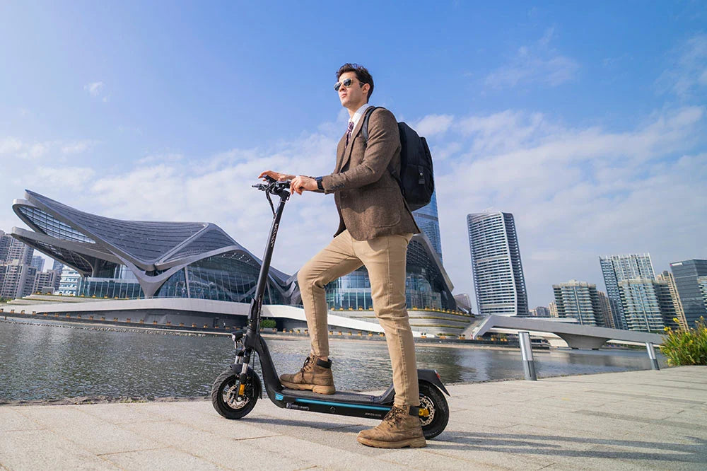 Businessman riding electric scooter along city waterfront with modern skyline background